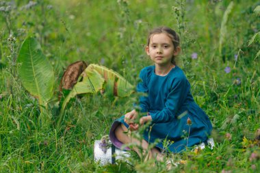 Genç bir kız canlı kır çiçekleriyle çevrili yemyeşil bir tarlada huzur içinde ve mutlu bir şekilde oturuyor.
