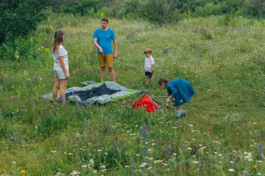Mutlu bir aile, çiçeklerle dolu yemyeşil bir arazide çadırlarını kurarak maceralı bir kamp yolculuğunun tadını çıkarır.