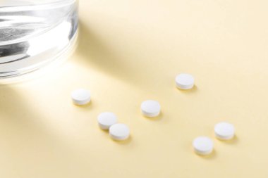 Tabletler masanın üzerinde, bir bardak suyun yanında. Vücudu vitamin ve beslenme takviyeleriyle desteklemek.
