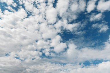 Kabarık beyaz kümülüs bulutlarıyla dolu, elektrik mavisi gökyüzü ile resmedilmiş doğal manzara, sakin bir atmosfer yaratıyor..