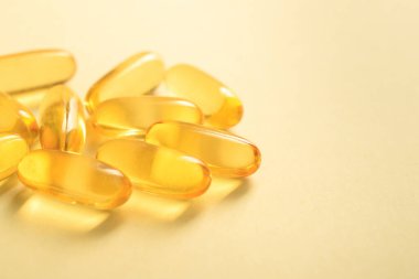 Sarı arka planda yumuşak jel kapsülünde bir avuç altın rengi yağ balığı yağı Omega-3 'ü kapat, boşluğu kopyala.