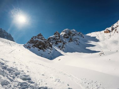 Üç pitoresk kayalık tepe parlak kış güneşinin gölgelerini karla kaplı yüksek dağ geçidine serer..