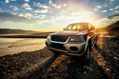 Gün doğumunda vahşi bir gölün yakınında, dağ yolunda bir off-road vagonu hazırlandı. Otomobille seyahat, vahşi yaşam macerası, keşif gezisi ya da 4x4 otomobille aşırı seyahat.