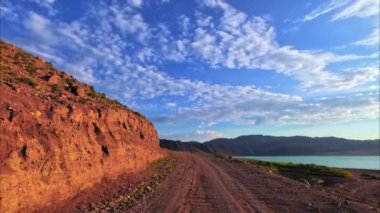 Resimli toprak yol, dinamik bulutlar ve yüksek dağlarla mavi gökyüzünün altında parıldayan Bartogay Gölü ile sınırdır. Kazakistan Doğası, Almaty Bölgesi