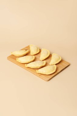 Tahta bir tahtanın üzerinde susamlı çiğ samosa. Geleneksel Türk yemekleri, dondurulmuş yarı bitmiş ürünler, kopyalama alanı.