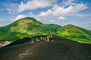 Bir grup turist koruyucu giysiler giyerek bir volkanı kumla kaplamak için hazırlık yapıyorlar.
