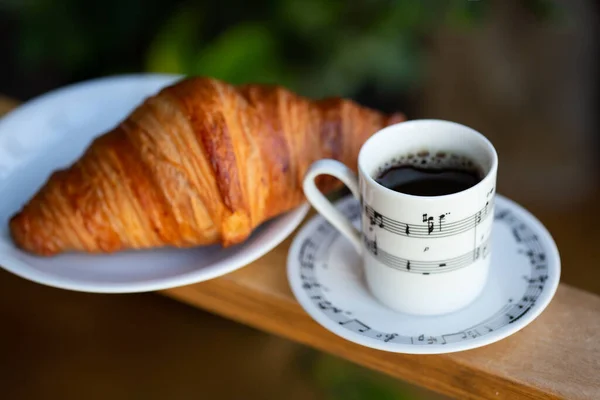 Closeup of musical notation and a coffee cup with croissant