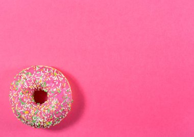 Pembe arkaplanda serpiştirilmiş pembe kremalı çöreğin üst görünümü, kopyalama alanı ile