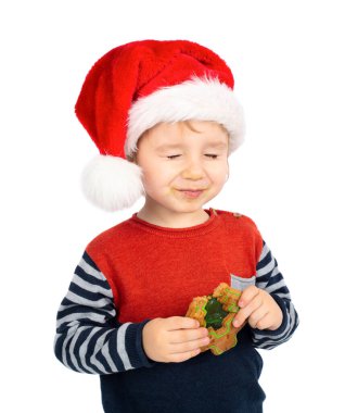 Noel Baba şapkalı küçük çocuk beyaz arka planda izole edilmiş Noel çöreği yiyor.