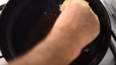 Bir adam sebze yağının döküldüğü tavaya çörek koyar..