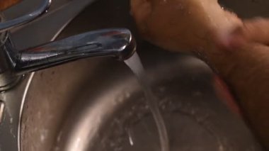 Adam ellerini köpürüyor. Adamın ellerinde köpük belirir. Adamın biri lavabodan akan bir su akıntısının altında temizler..