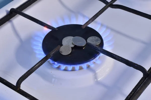 Close-up of a gas stove burner. Burning gas. There is metal money on the burner, a symbol of an expensive gas price.