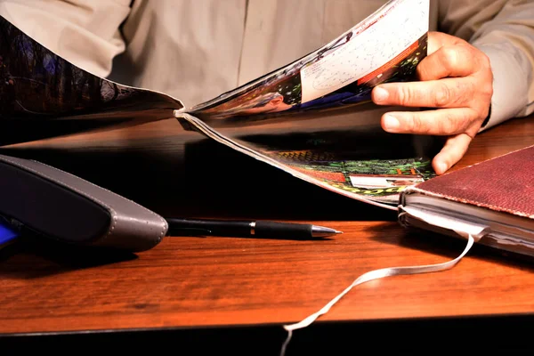 写真にはテーブルに座って雑誌を手に取り読書している男が写っている — ストック写真