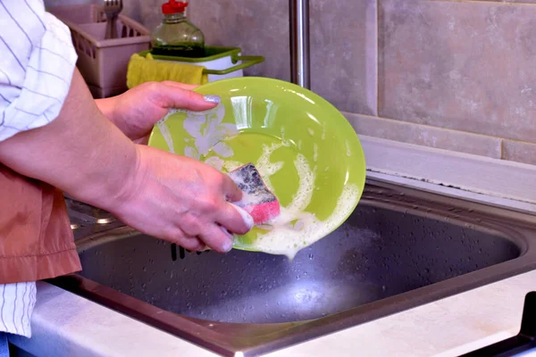 一个女人一边拿着盘子 一边用海绵和洗涤剂洗碗 — 图库照片