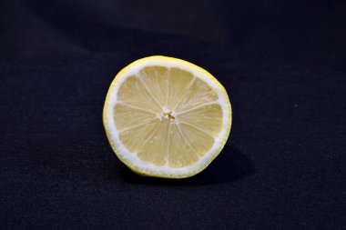 Sarı sulu bir limonun yarısı koyu bir arka planda yatıyor..