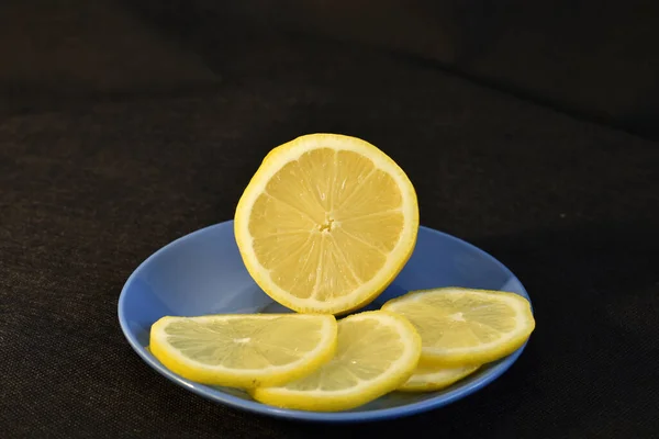 半块黄色的多汁柠檬和几片水果放在蓝色的盘子里 背景是漆黑的 — 图库照片