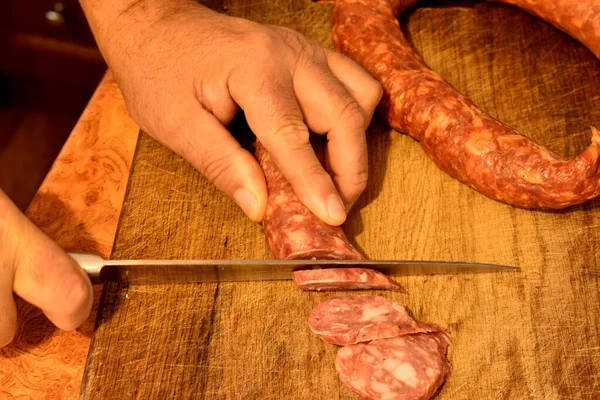 stock image Top view of male hands cutting sausage on a cutting board with a knife.