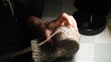 Kadın masada oturuyordur. Masa lambası yanıyor. Kadın eli, yün çorapları iğne iplikle onarıyor..