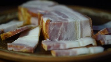 Büyük bir parça jambonun yakın plan görüntüsü ve kesikleri bir tabakta duruyor, dönüyor..