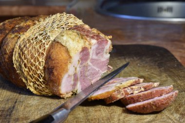 Büyük bir parça jambon, bir bıçak ve doğranmış et kesme tahtasının üzerinde yatıyor..