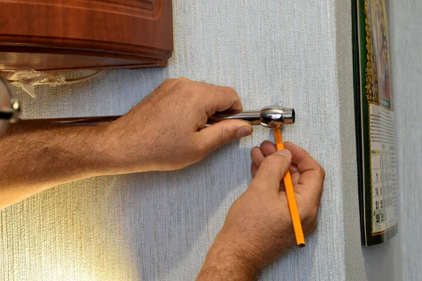 The picture shows men\'s hands, which make markings with a pencil for a hole on the wall.