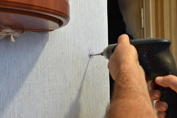 The picture shows men's hands, which are drilling a wall with a drill.