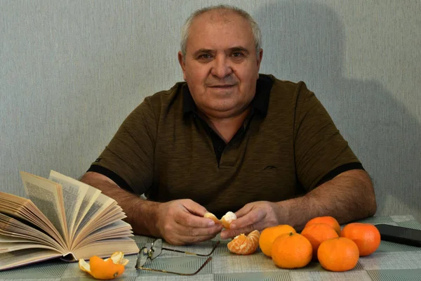 Mies Istuu Pöydän Ääressä Hänen Edessään Kirja Appelsiineja Hän Kuori — kuvapankkivalokuva