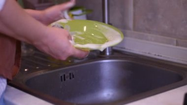 Video, bir kadının tabağı elleriyle nasıl yıkadığını gösteriyor. Bunun için sünger ve deterjan kullanıyor..