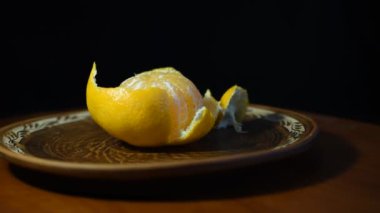 Kabuğu soyulmuş bir portakal, kilden bir tabakta yatıyor. Tabak dönüyor..