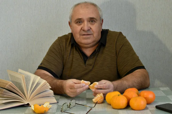 Mies Istuu Pöydässä Kuorii Appelsiineja Käsillään — kuvapankkivalokuva