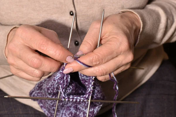 Women\'s hands are knitting a warm sock with four knitting needles.