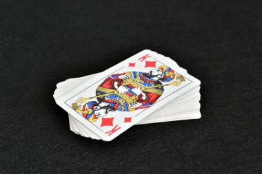 Karanlık masada bir deste poker kartı unutulur. Karo papazı üstte.