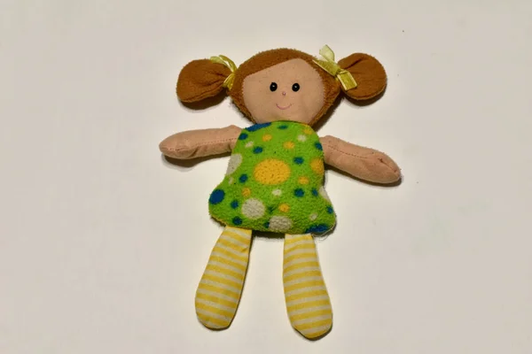 On a light background is a soft toy, in a green dress and with pigtails.