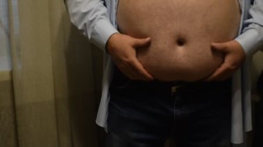 Adam koca göbeğini elleriyle sallıyor. Rejime ihtiyacı var. Adam aşırı kilolu..