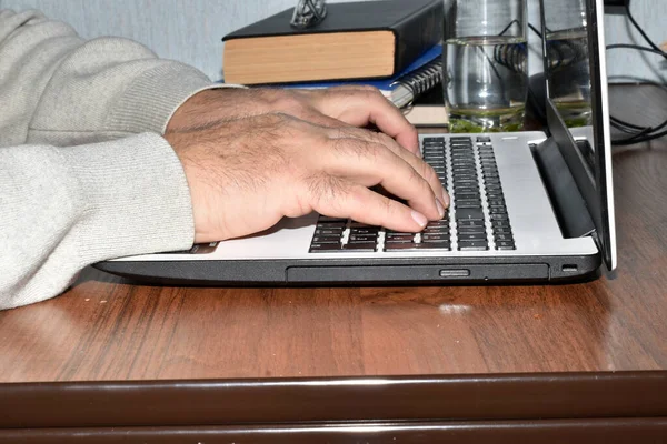 Side view of a man, his hands, which is typing text on a laptop.