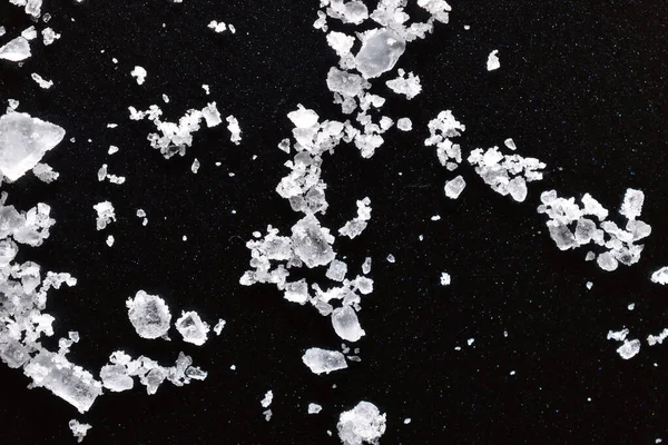 Transparent crystals of rock salt are scattered on the surface of a dark table.