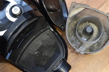 On the floor are parts of a disassembled vacuum cleaner, a body, a dust collector and a cover from the device.