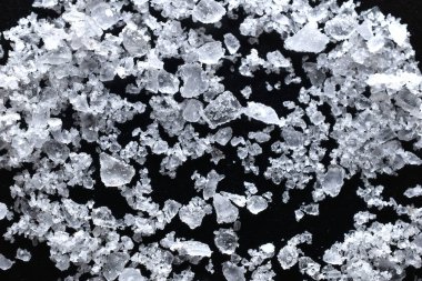 Texture pattern created by transparent white salt crystals scattered on a dark table.