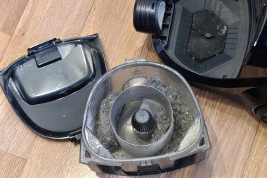 There is a vacuum cleaner on the floor, and parts taken out of it lie nearby.