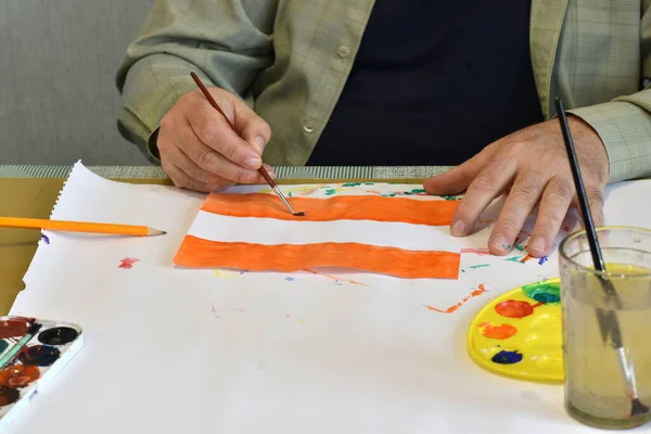 The picture shows the artist\'s hands, which draw the flag of Austria with a brush and watercolors on paper.