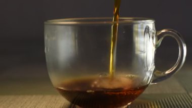 A thin stream of tea is poured into a glass transparent cup.