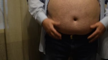 An elderly man shakes his fat huge belly with his hands.