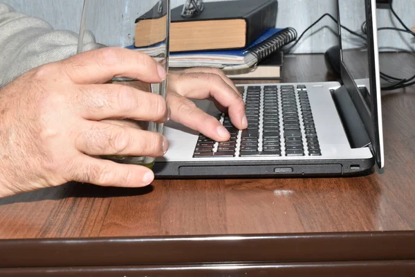 The picture shows a man typing on a laptop keyboard with one hand and holding a glass of water in the other.