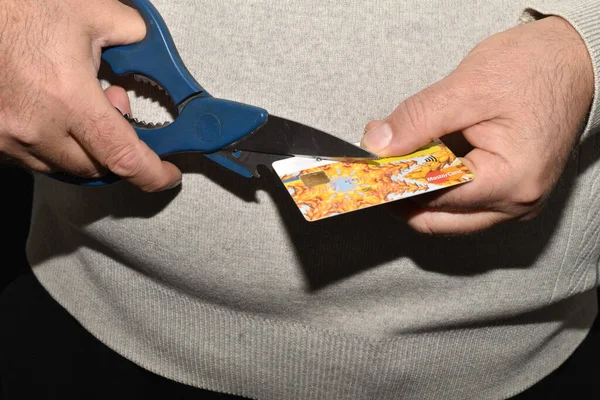 The picture shows a man holding a bank card with one hand and scissors with the other.