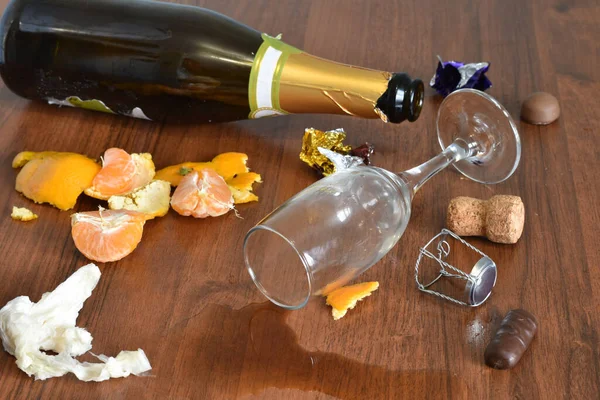 After a fun holiday, a bottle, a glass with spilled wine and a peel from tangerines remained on the table.