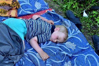 The picture shows a child sleeping in the garden on a mattress and blankets, close-up.