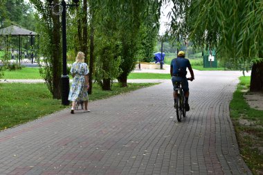 Tambov. Tambov Region. Russia. 09/08/2021. City Park. A woman walks along a path in a park, a cyclist catches up with her.