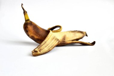 On a white background lies a banana that has not been completely peeled. The banana peel has dark spots. The banana is overripe.
