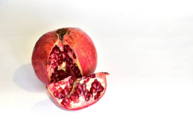 Pomegranate and its cut slice with red grains lies on white.
