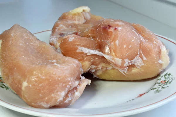Chicken frozen meat covered with ice lies on a plate.